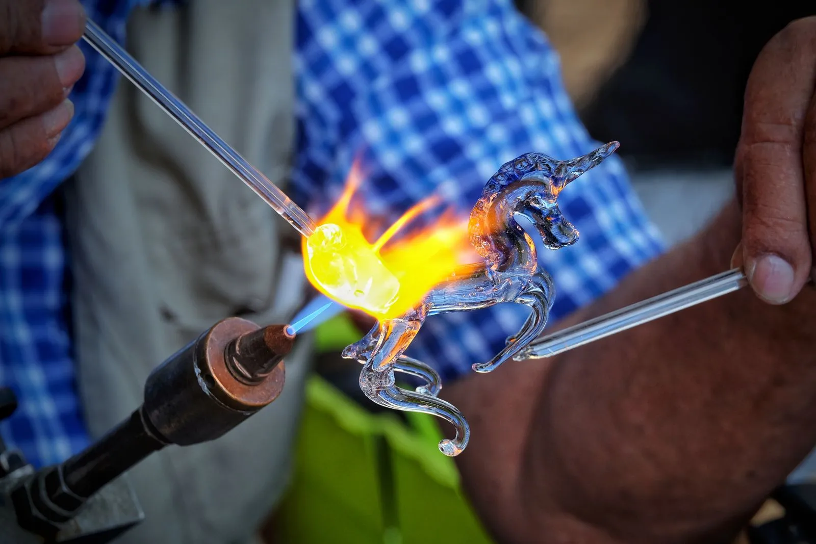 Artisan using a flame to craft a delicate glass unicorn sculpture. Close-up view of intricate glassblowing technique.